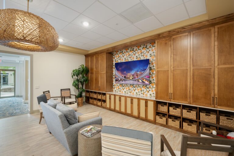 A cozy lounge with a sofa, armchairs, a wicker light fixture, built-in wooden cabinets, woven storage baskets, a plant, and a wall-mounted TV displaying a city bridge at night.