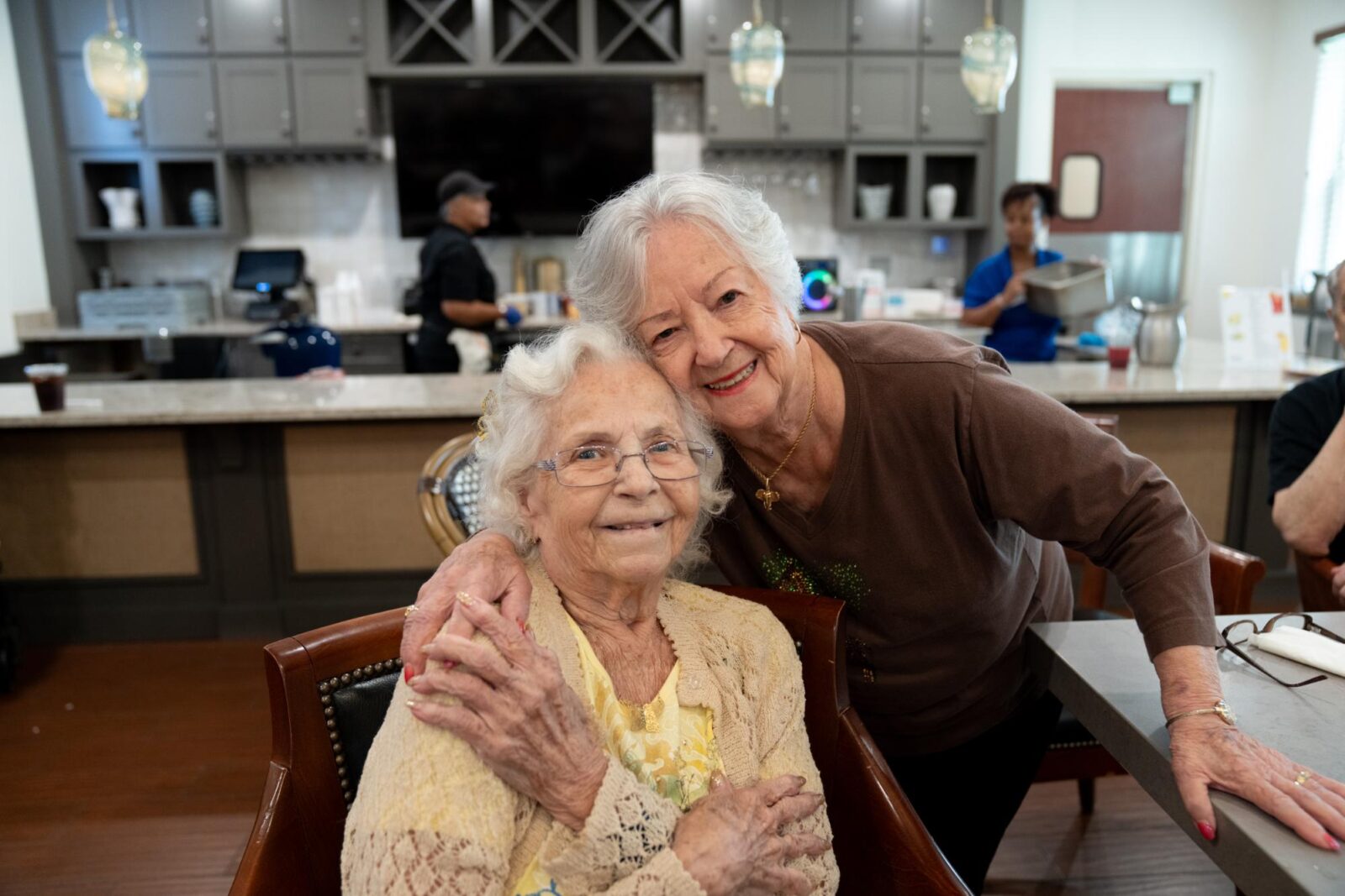 Two smiling residents at The Glades at ChampionsGate share a warm embrace inside the community café.