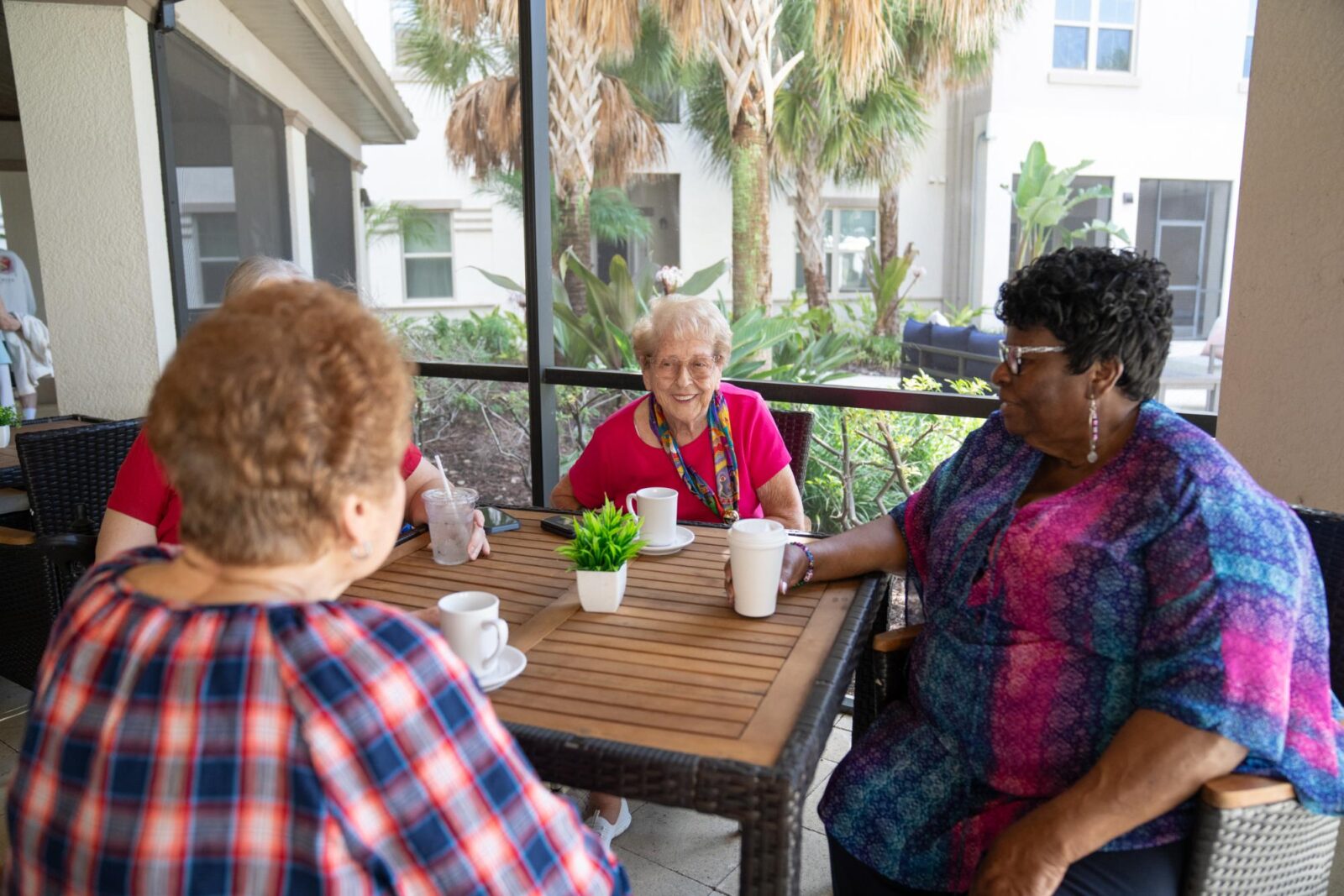 A group of older adults sitting together at a senior living community, enjoying coffee and conversation in a relaxed patio setting.