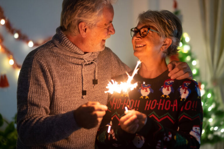 A joyful older man and woman smiling and connecting while holding sparklers to celebrate Christmas