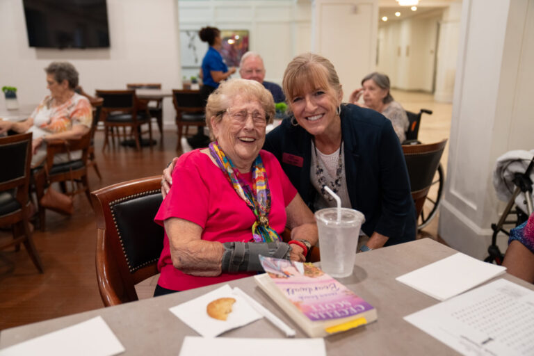 Senior resident smiling alongside a team member at The Glades at ChampionsGate, a senior living community near Orlando, Florida.